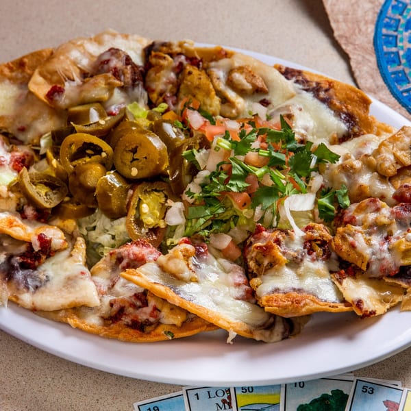 A plate of Homemade Taqueria's nachos, topped with melted cheese, jalapeños, pico de gallo, and meat.