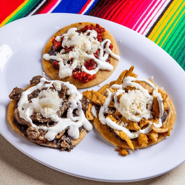 Three Homemade Taqueria sopes with various toppings, crema, and cheese on a white plate.