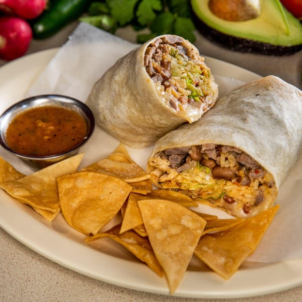 Two Homemade Taqueria burritos, one cut open, with tortilla chips and salsa on a plate.